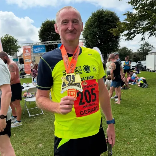 Gerard holding a marathon finisher medal in his running kit
